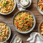 Elegant spread of rotisserie chicken dishes including creamy pasta, grain bowl, and enchiladas arranged on rustic wooden table with fresh herbs